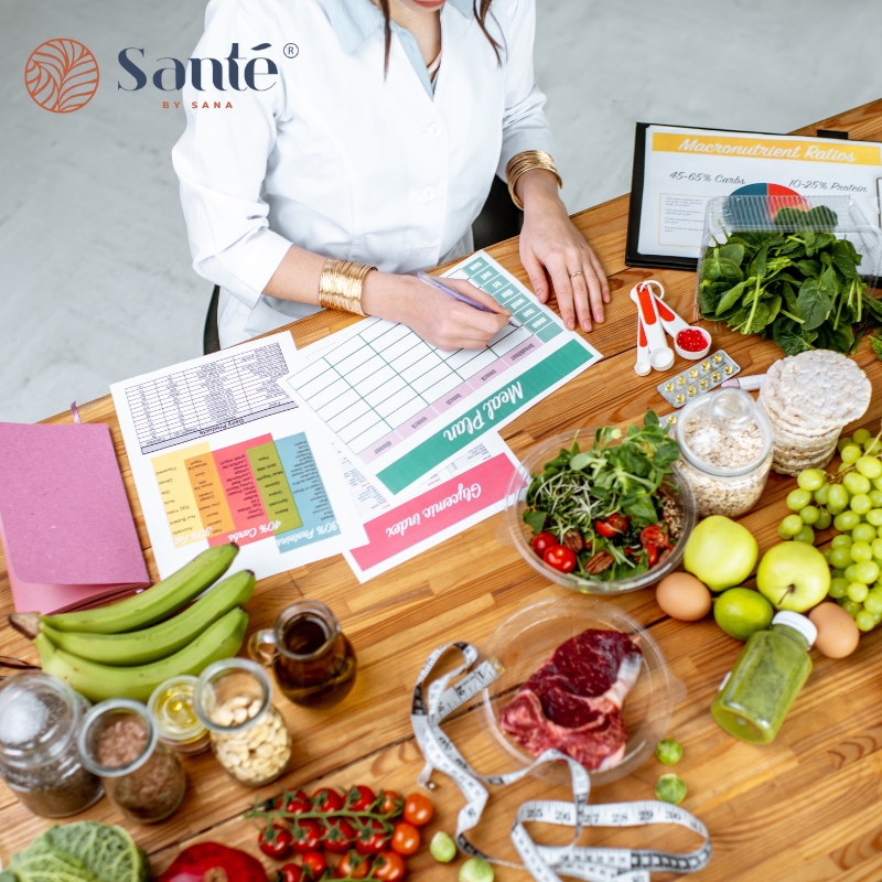 Dietitians in Acacia Gardens planning healthy meals with charts, fresh fruits, vegetables, meat, grains, and nutritional guides on the table.